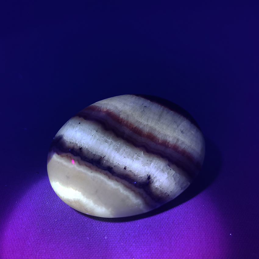 Pink aragonite premium grade worry stone under UV light
