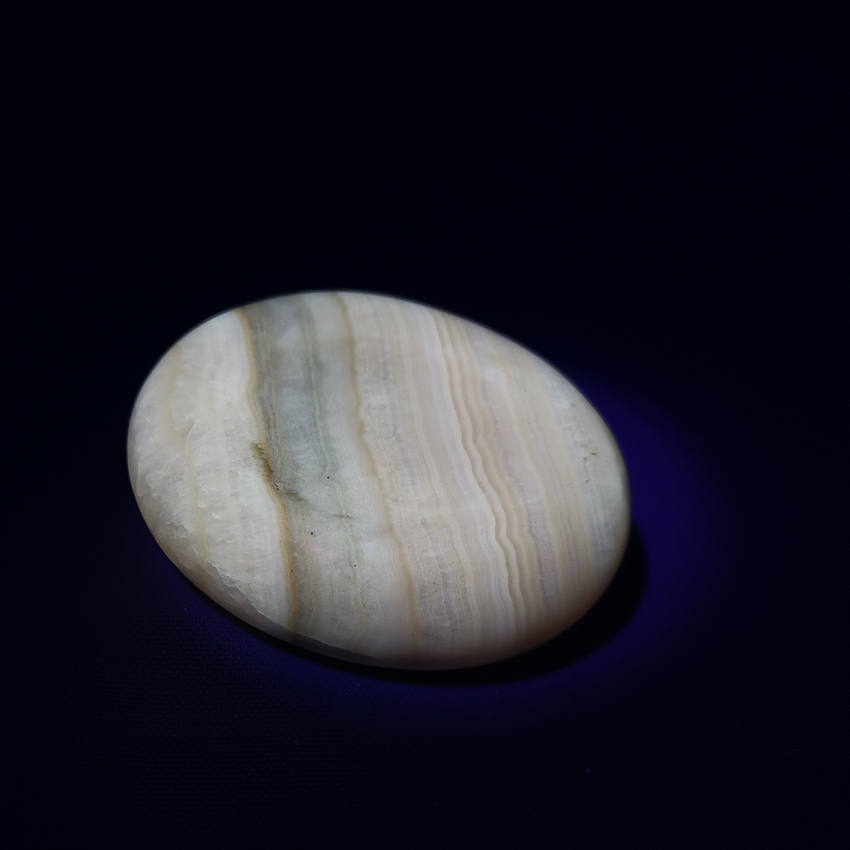 coati aragonite worry stone under UV light